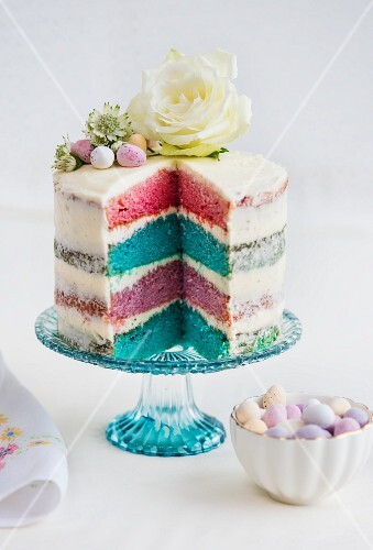 A four-layer rainbow cake with white frosting, Easter eggs and flowers (sliced)