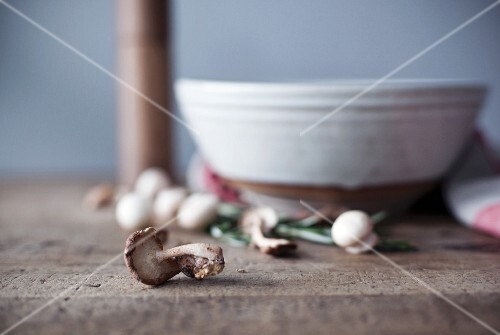 An arrangement of fresh mushrooms with a ceramic bowl in the background