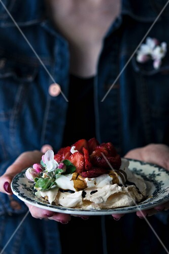A woman holding a strawberry pavlova with cream and Crema di Balsamico in her hands